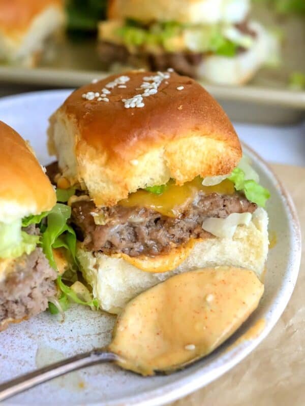 Up close photo of a big mac slider on a white plate with a saucy spoon.