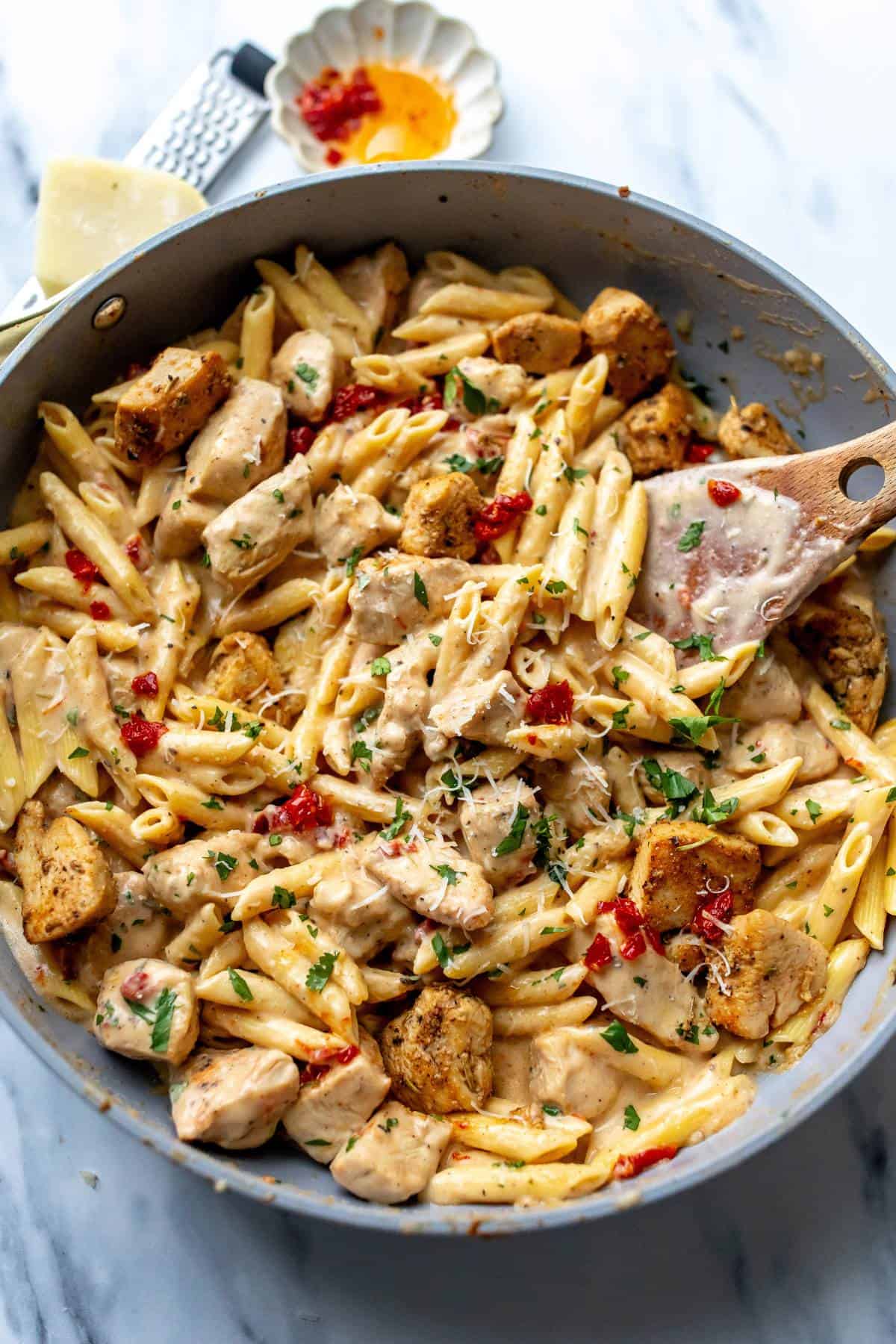 Grey skillet with marry me chicken pasta in it and a wooden spatula in the skillet. 