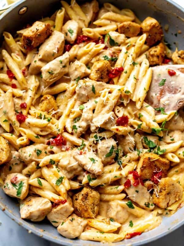 Grey skillet with marry me chicken pasta in it and a wooden spatula in the skillet.