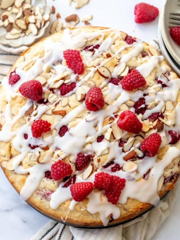 Raspberry Almond Cake on a white counter with raspberries and icing and forks to the side.