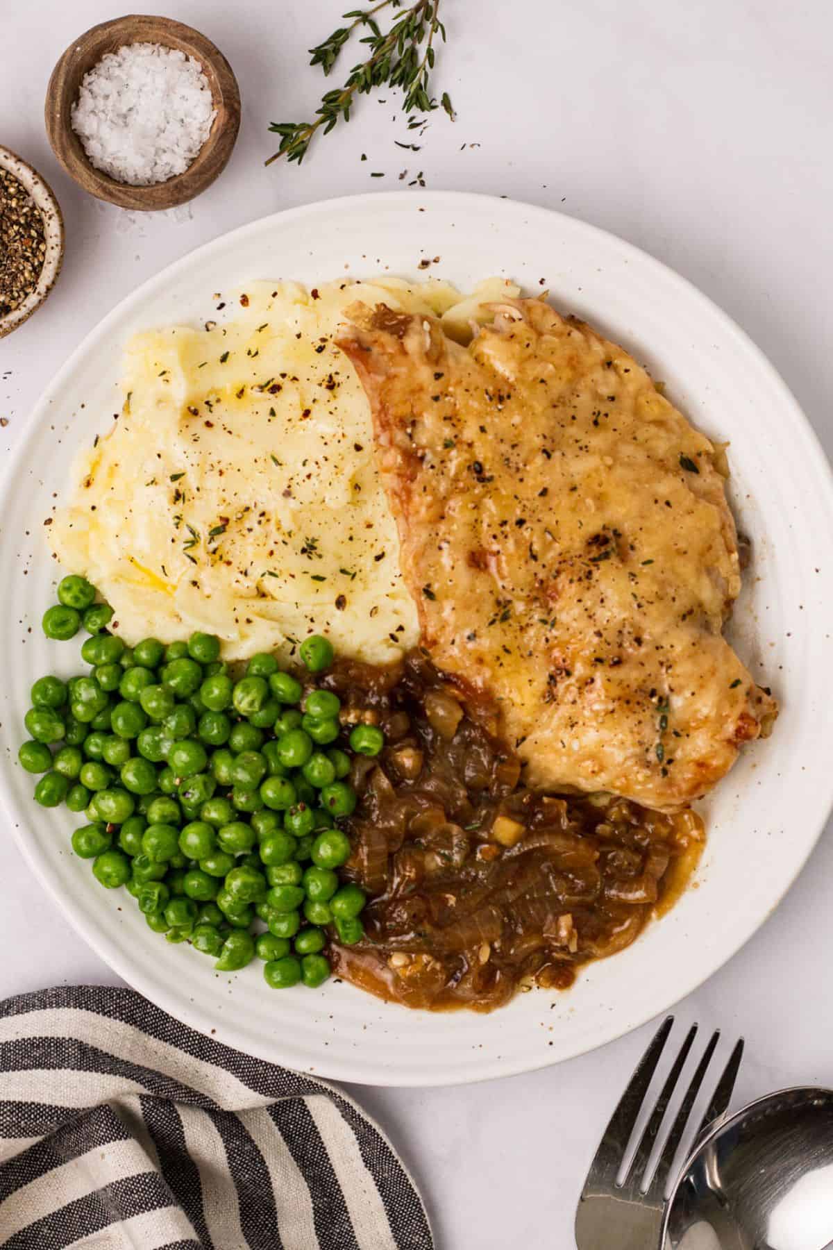 White ceramic plate with French onion soup chicken and peas and a  fork to the side. 