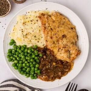 White ceramic plate with French onion soup chicken and peas and a fork to the side.