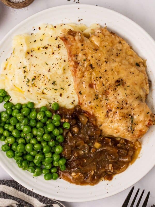 White ceramic plate with French onion soup chicken and peas and a fork to the side.