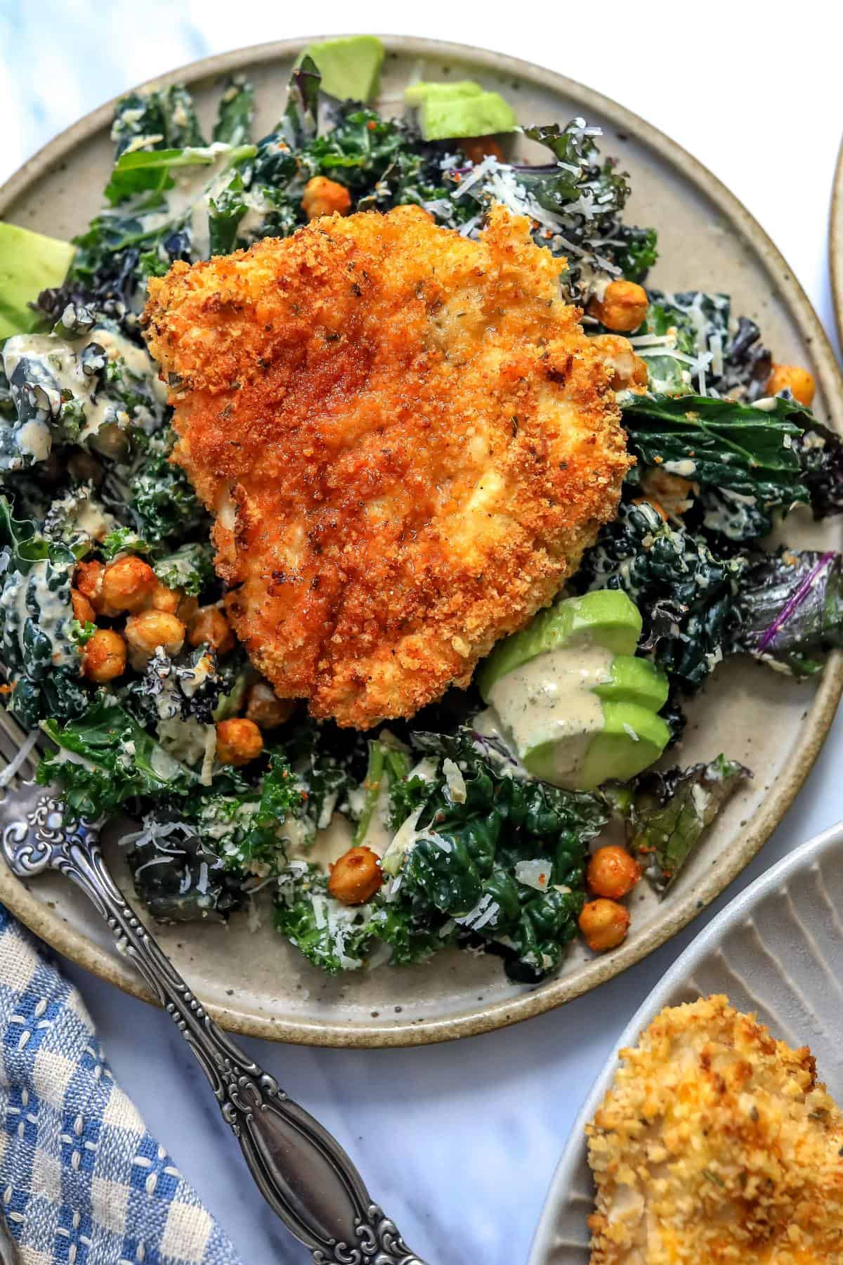 An overhead image of serving chicken cutlets with lemon kale Caesar salad.