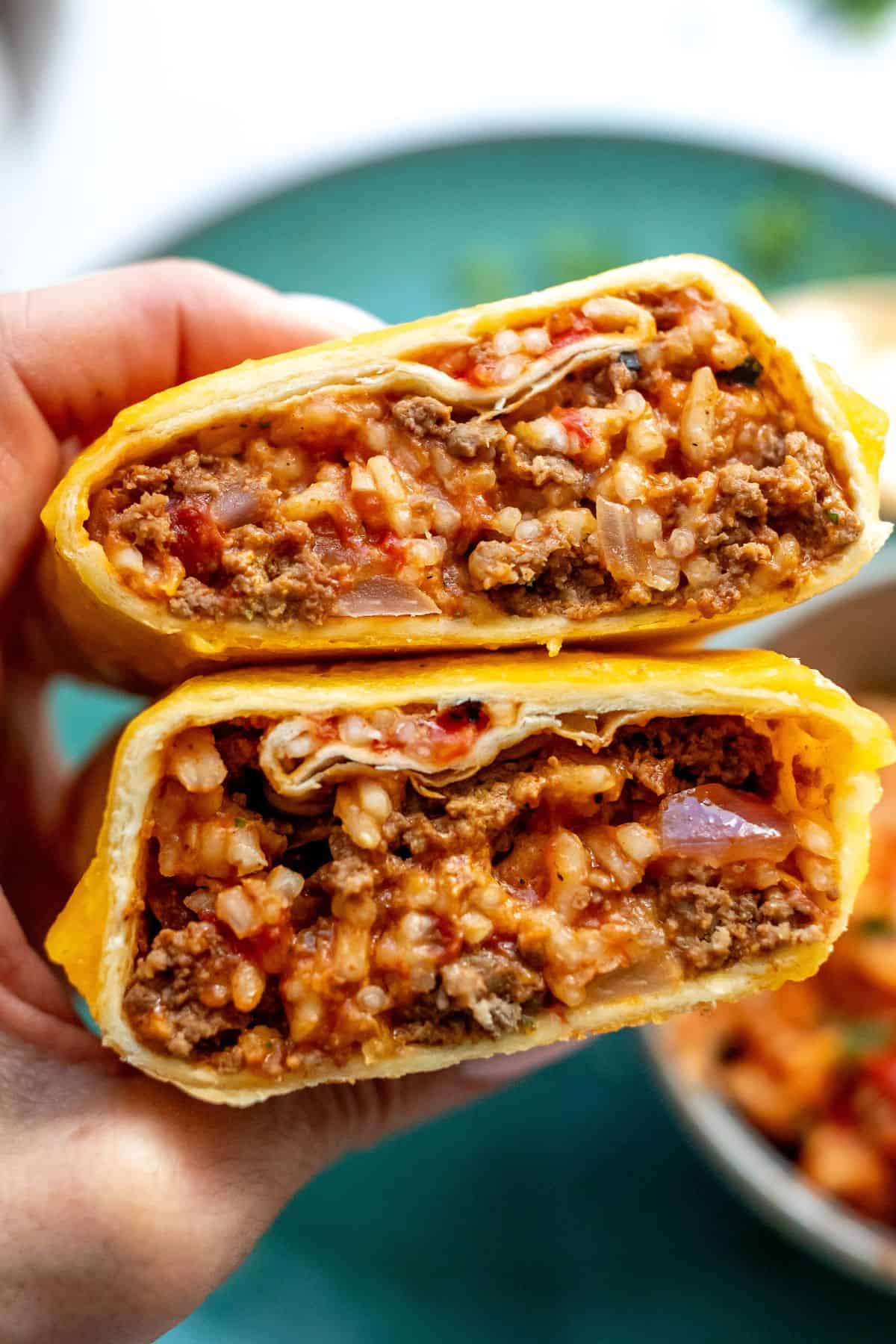A close up image of a person holding two grilled cheese burritos over each other.