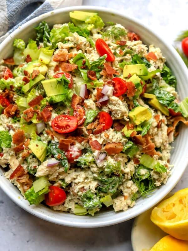 BLT Chicken Salad in a white ceramic bowl with tomatoes and bacon on top.