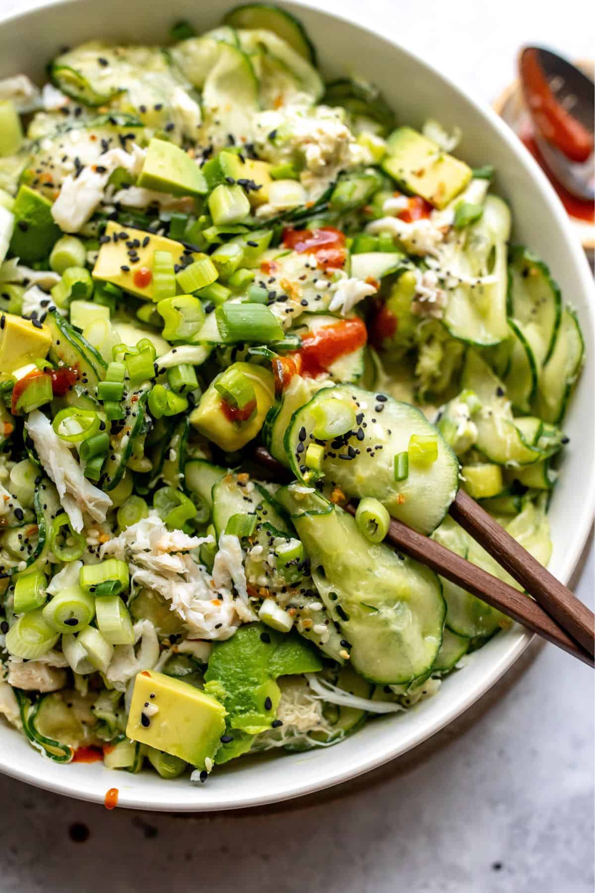 White bowl filled with California Roll Cucumber Salad with a drizzle of sriracha on top.