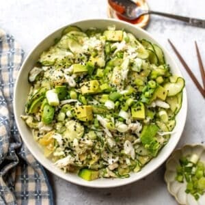 White bowl with filled with California Roll Cucumber Salad. Avocados on top with sesame seeds.