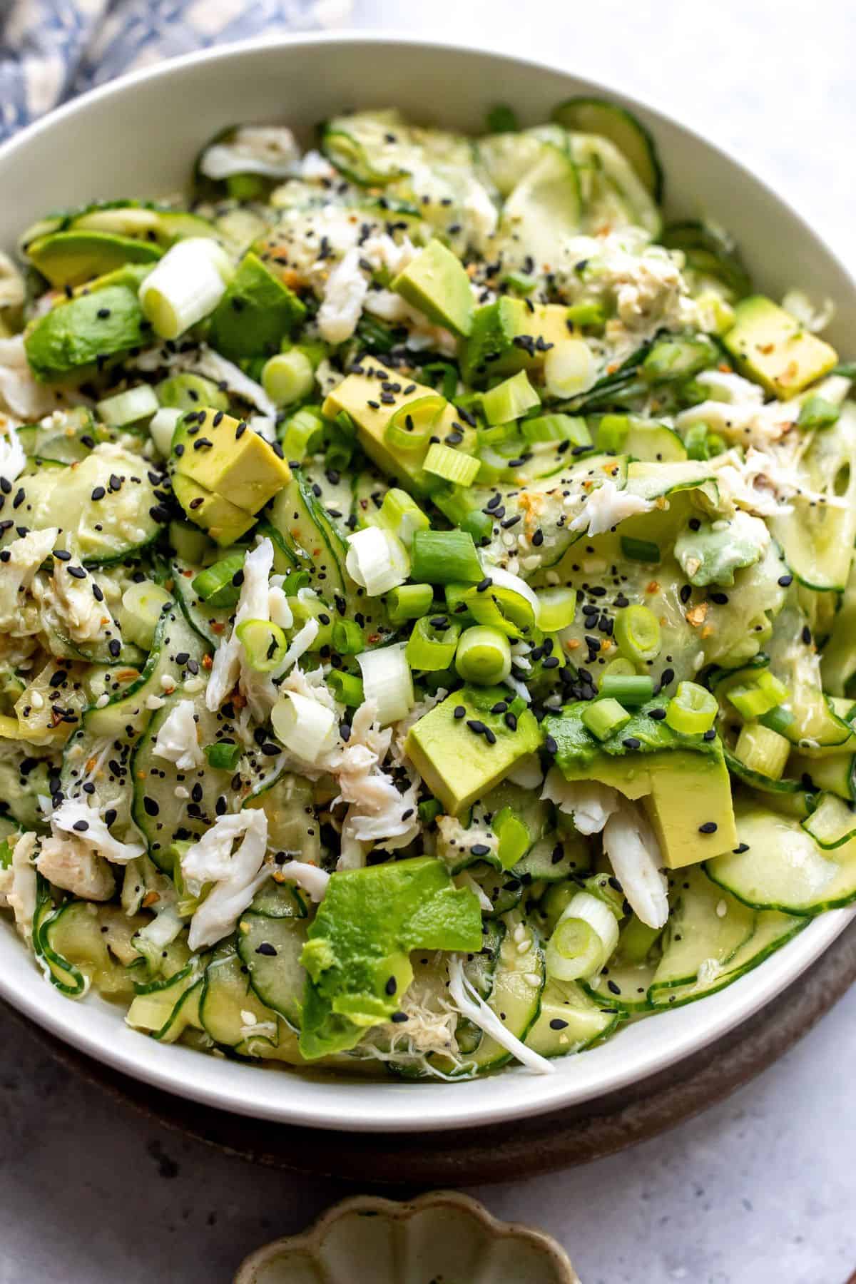 White bowl filled with California Roll Cucumber Salad. Avocados on top with sesame seeds.
