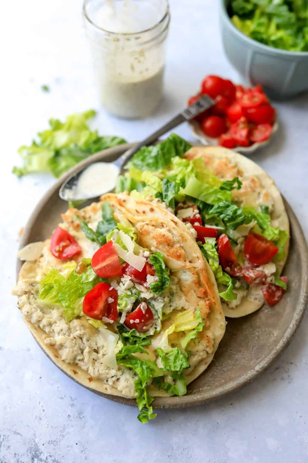 Chicken Caesar Smashed Tacos on a grey plate with dressing on the side and a spoon. 