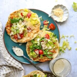 Chicken Caesar Smashed Tacos on a green plate with dressing on the side and a spoon.