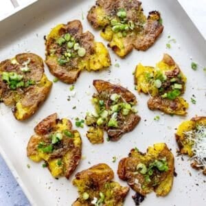 Crispy smashed potatoes on a baking sheet with green onions and cheese.