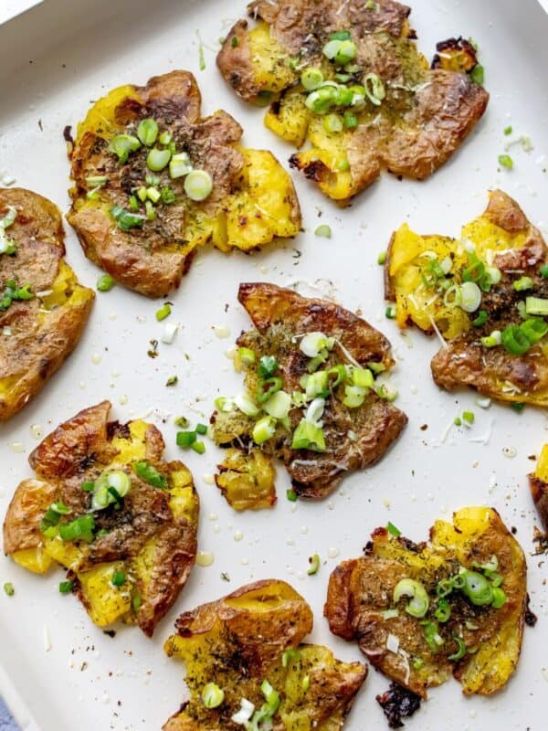 Crispy smashed potatoes on a baking sheet with green onions and cheese.