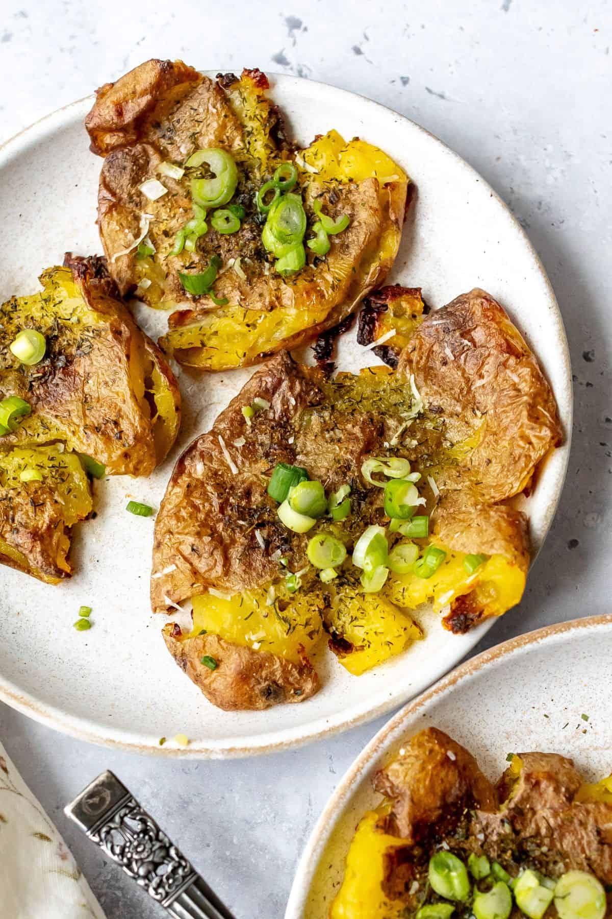 Smashed potatoes with crispy edges on a white plate.