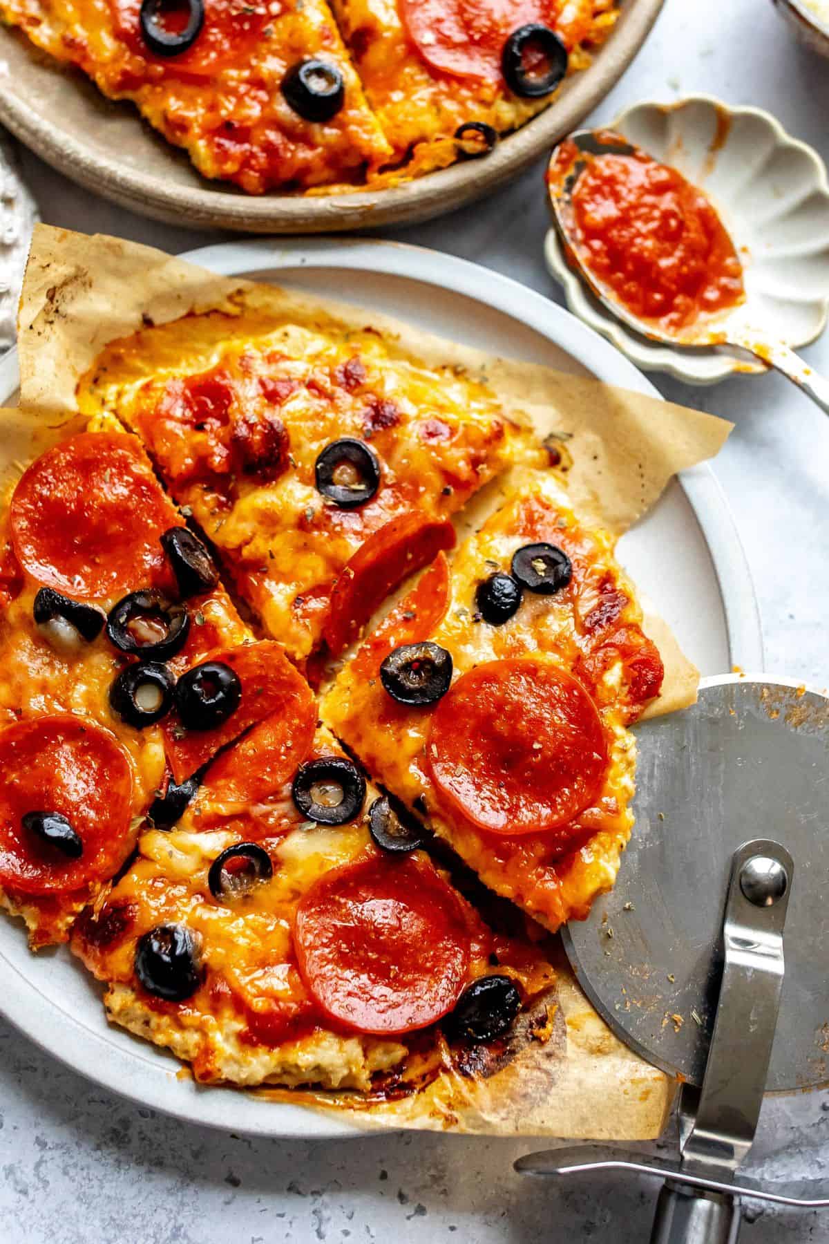 Up close photo of chicken crust pizza with pepperonis on it and a pizza cutter.