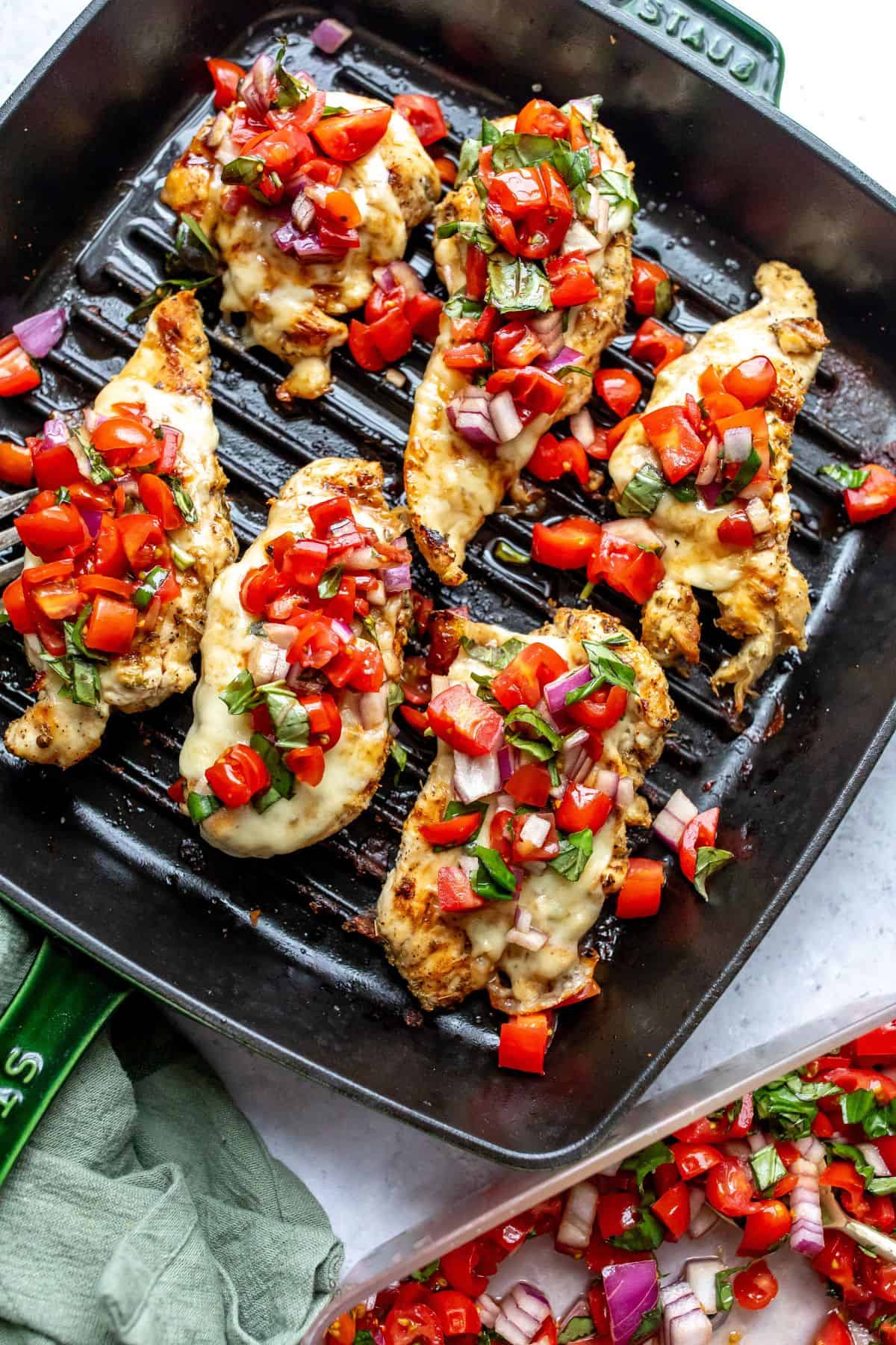 Grill pan with grilled chicken caprese on it and tomatoes to the side.