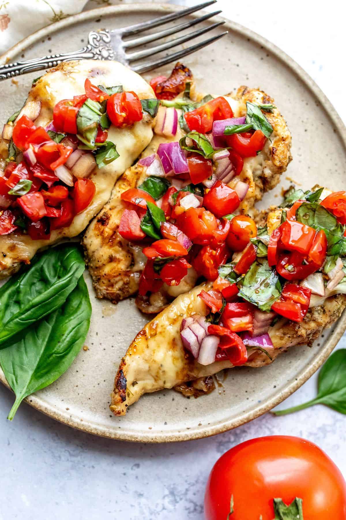 A ceramic plate with speckles with Grilled Caprese Chicken on it and lots of basil.