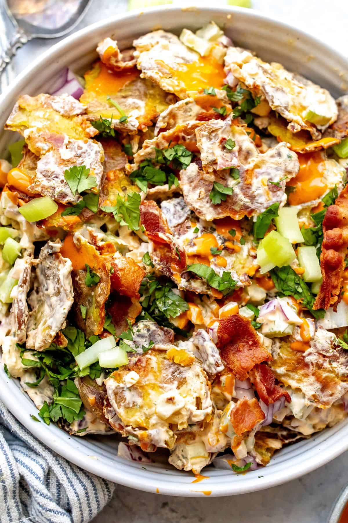 Smashed Buffalo Potato Salad in a white bowl with bacon.
