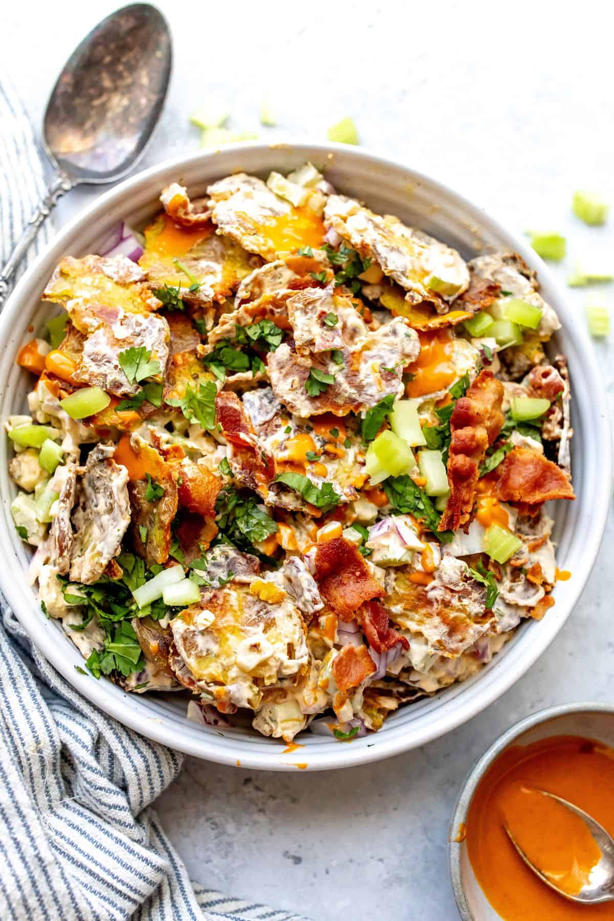 Smashed Buffalo Potato Salad  in a white bowl with a silver spoon. 