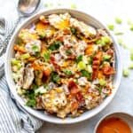 Smashed Buffalo Potato Salad in a white bowl with a silver spoon and a lemon on the side.
