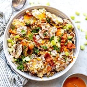 Smashed Buffalo Potato Salad in a white bowl with a silver spoon and a lemon on the side.