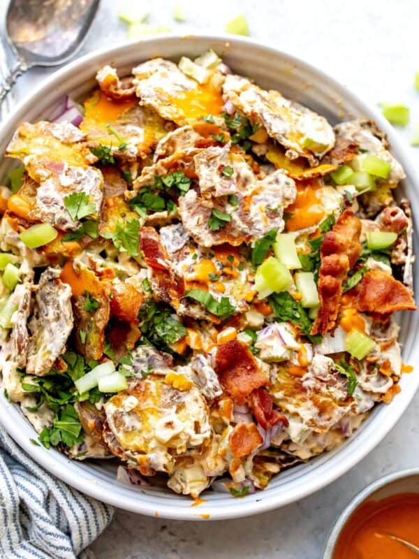 Smashed Buffalo Potato Salad in a white bowl with a silver spoon and a lemon on the side.