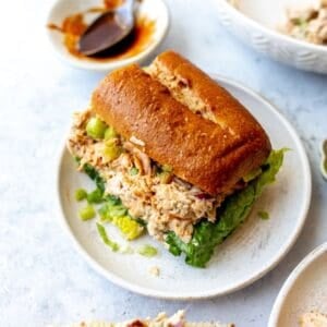 White plate with Smoked Chicken Salad on wheat buns with bbq sauce on the side.