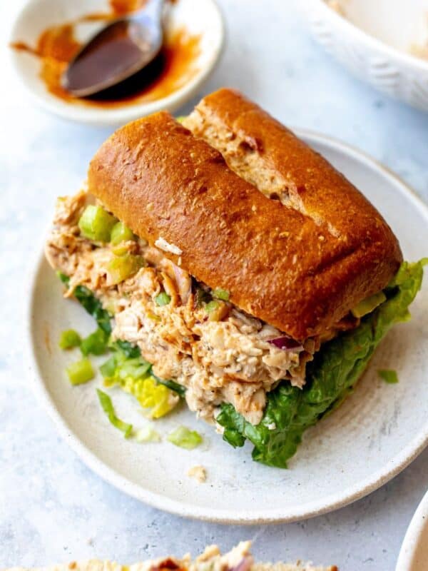 White plate with Smoked Chicken Salad on wheat buns with bbq sauce on the side.