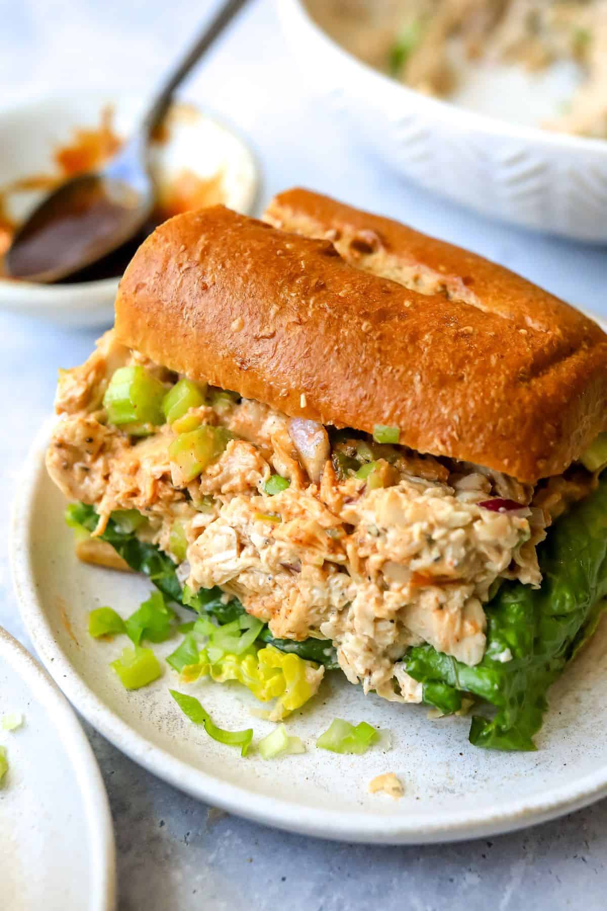 White plate with Smoked Chicken Salad on wheat buns with bbq sauce on the side.