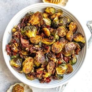 White bowl with Balsamic Honey Brussels Sprouts and honey on the side.