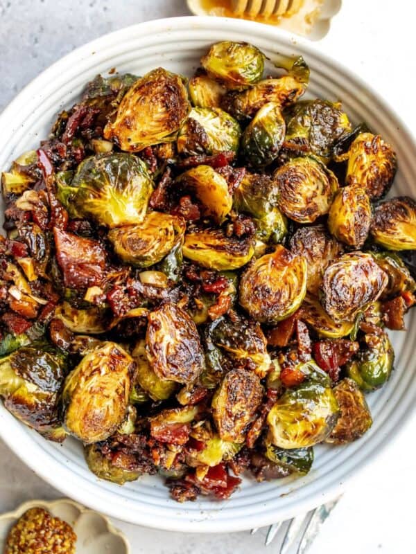 White bowl with Balsamic Honey Brussels Sprouts and honey on the side.