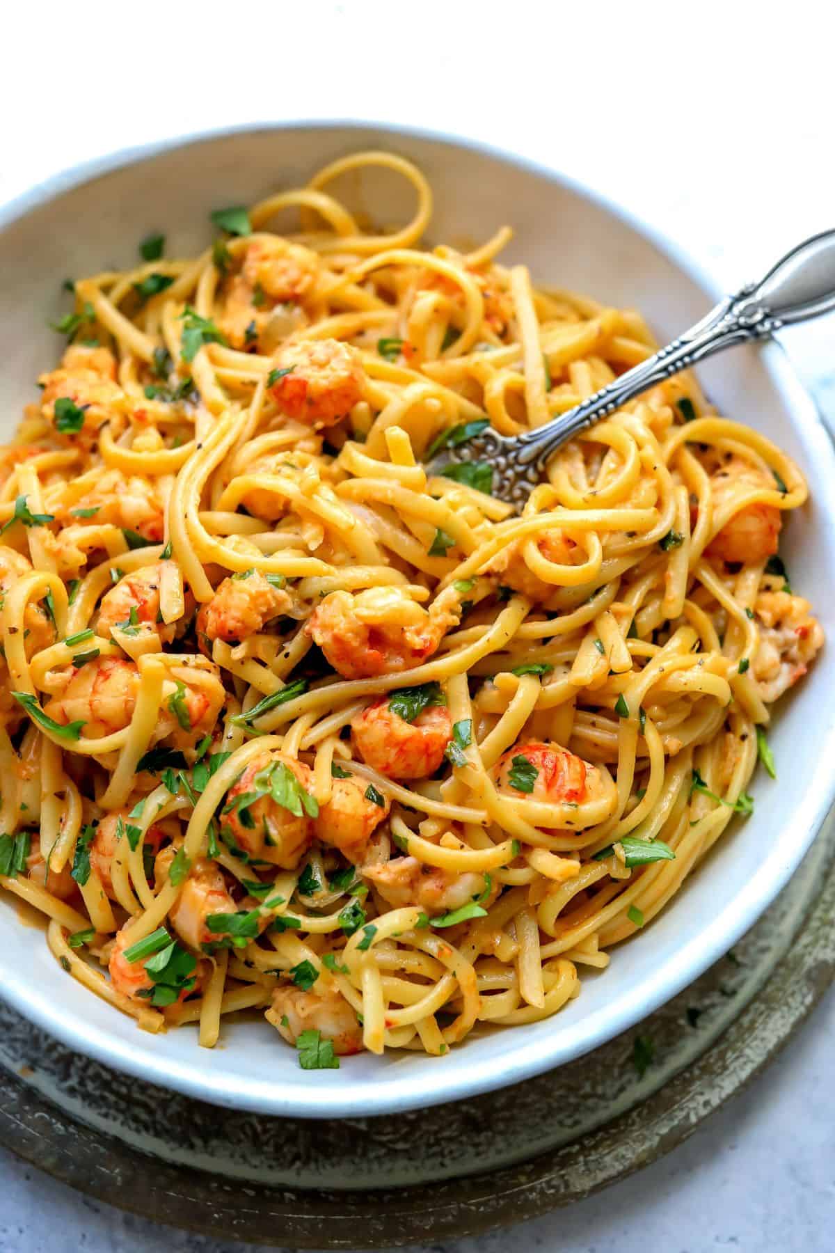 White bowl with lobster pasta in it and a silver fork.