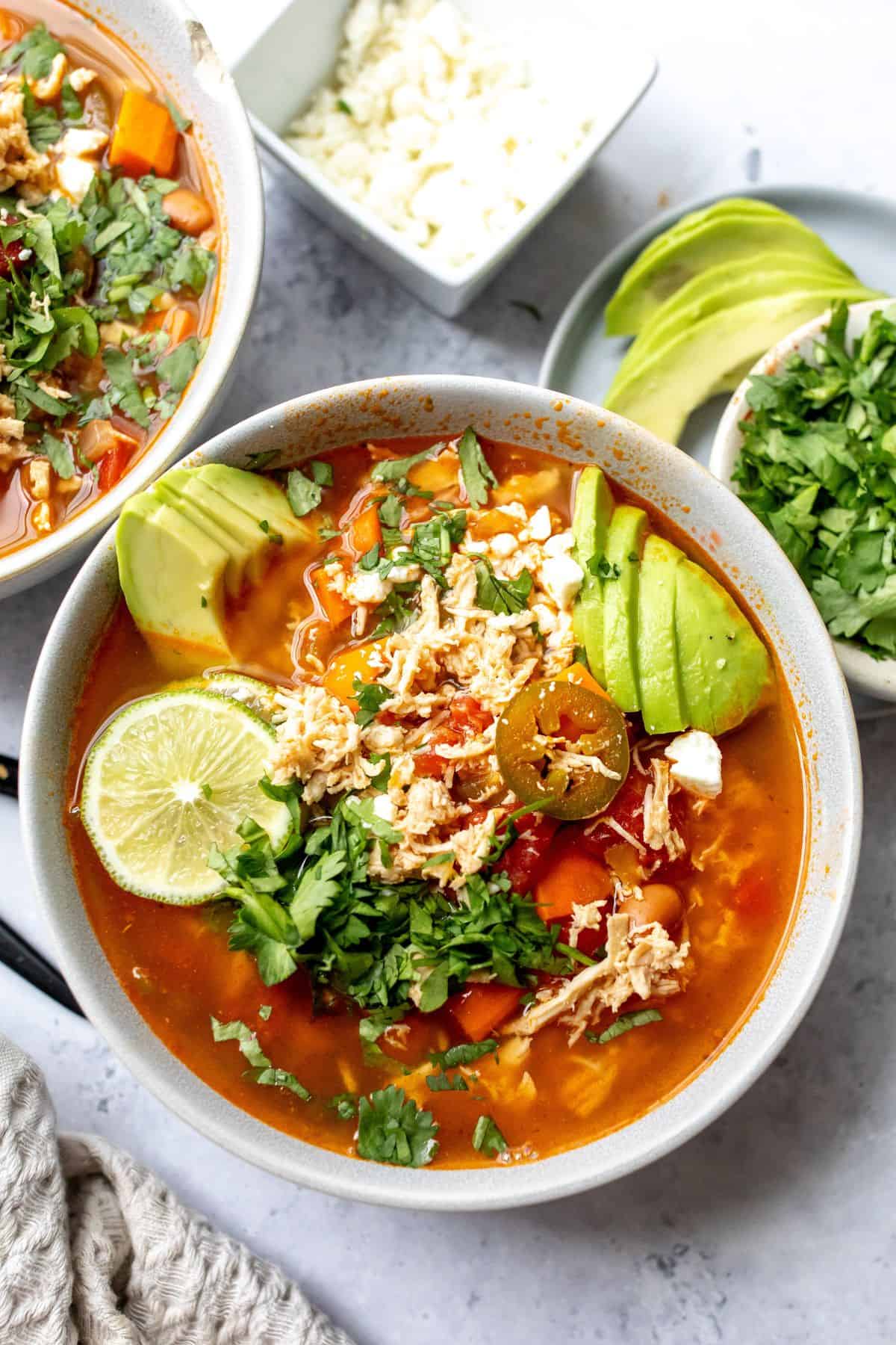 Ceramic bowl with brothy Mexican Chicken Lime Soup Recipe and fresh limes.