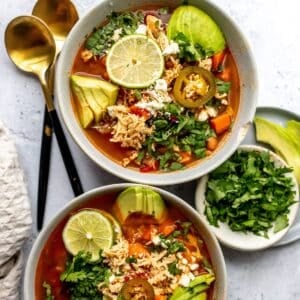 Mexican Chicken Lime Soup in two ceramic bowls with avocado and lime.
