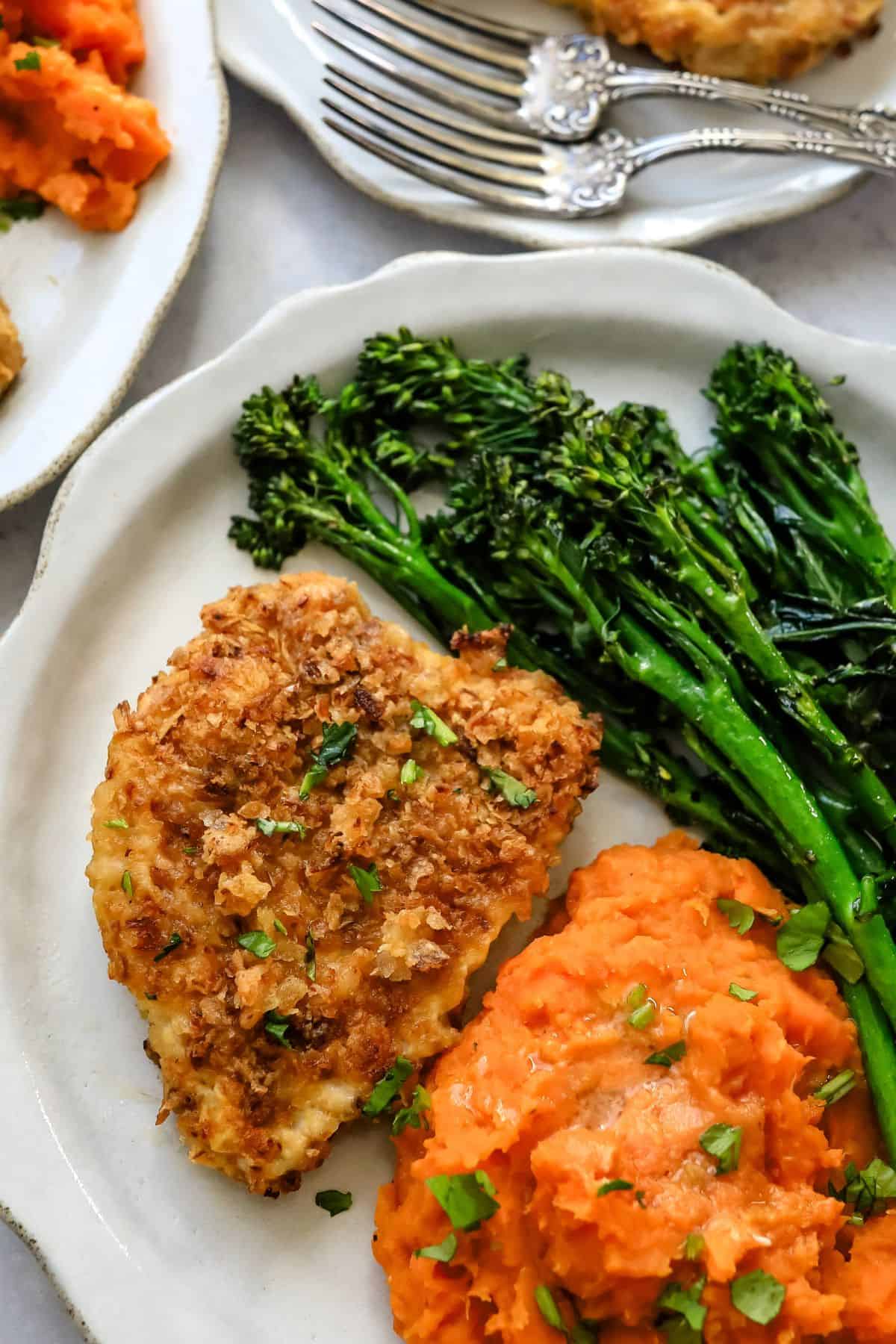 Baked pork chops on a white plate with broccoli and sweet potatoes.