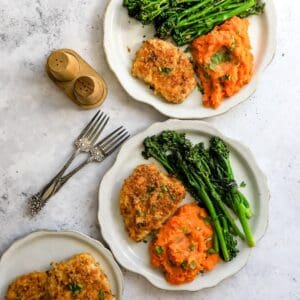 Baked pork chops on a two white plate with broccoli and sweet potatoes.