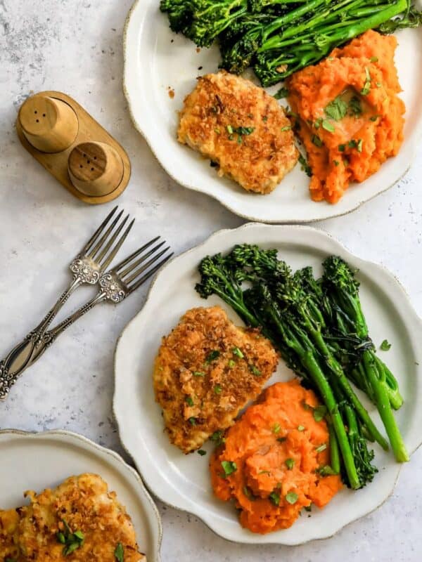 Baked pork chops on a two white plate with broccoli and sweet potatoes.