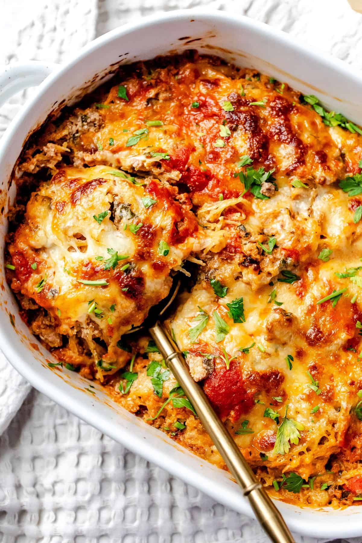 White ceramic baking dish with Spaghetti Squash Lasagna in it and a spoon on the side. 