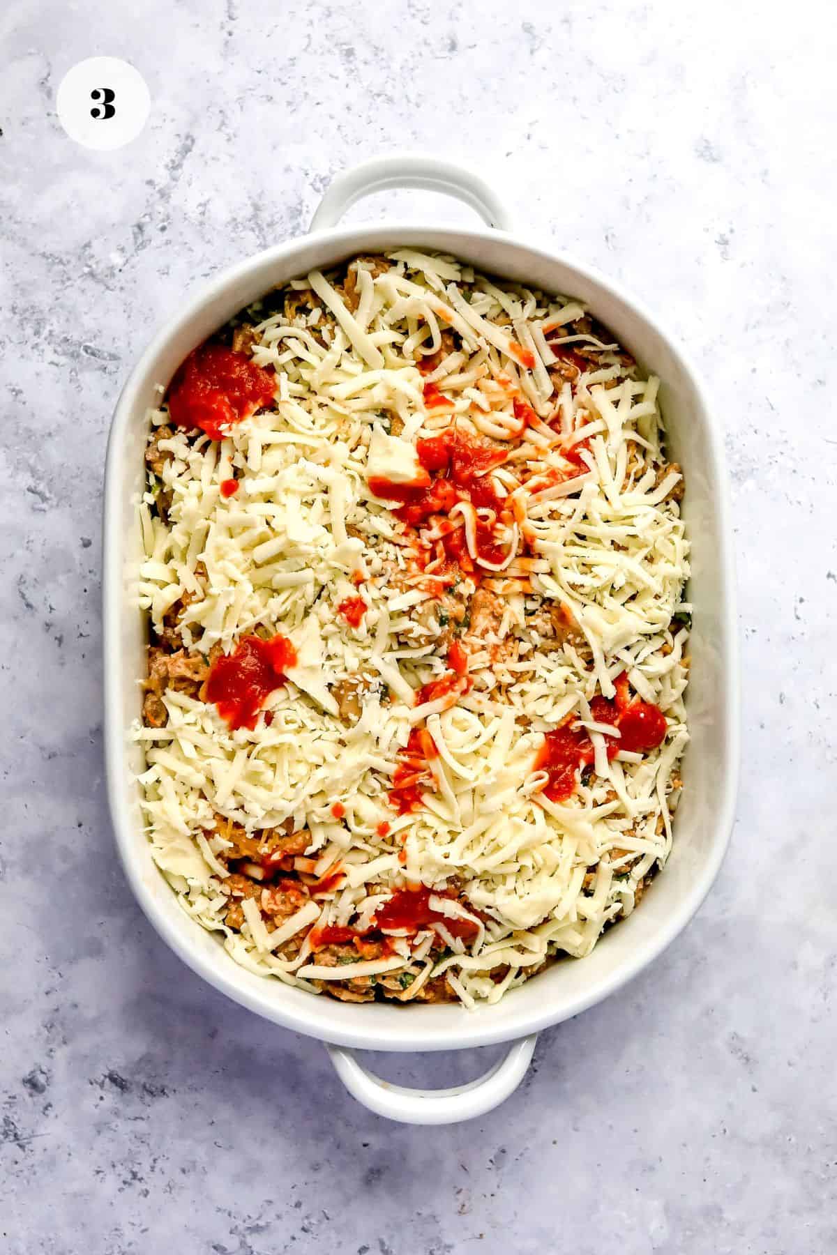 White ceramic dish with lasagne mix and shredded cheese. 