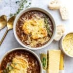 Two bowls with healthy french onion soup in them, gold spoons off to the side and cheddar shredded.