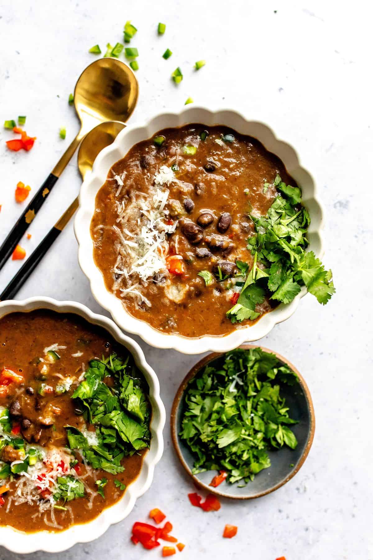 White ceramic bowl with Panera Black Bean Soup Recipe in the bowl with two spoons to the side.
