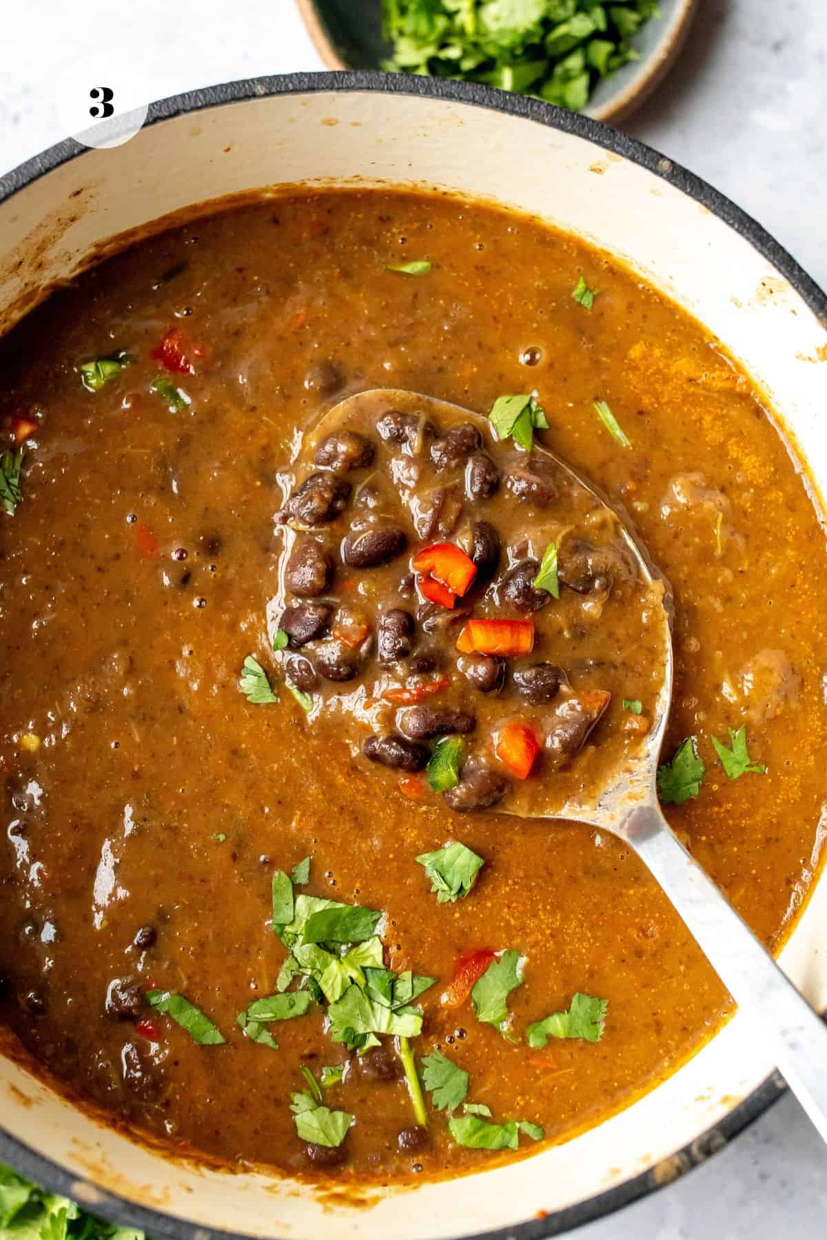 Large soup pot with black bean soup with a serving spoon in it and cilantro.