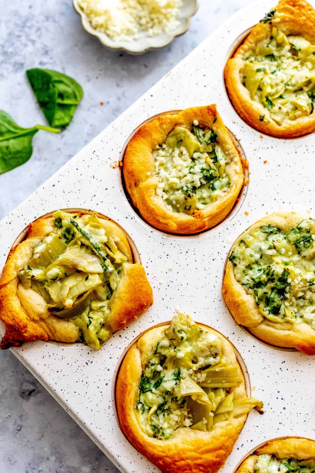 White muffin tine with Spinach Artichoke Bites in it, up close photo of them baked.