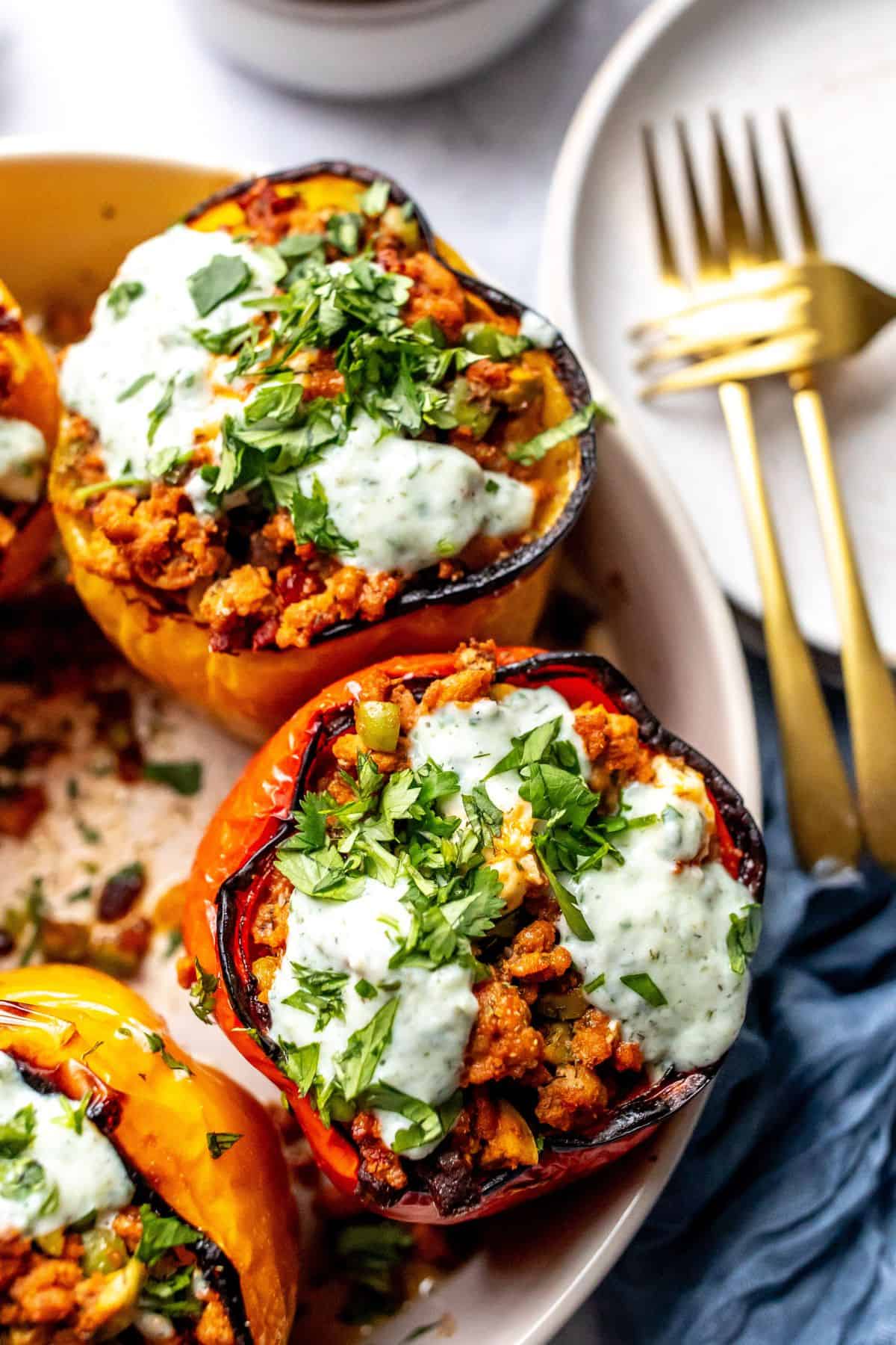 Ground turkey stuffed Peppers in a grey bowl with gold forks and plates on the side. Up close photo. 