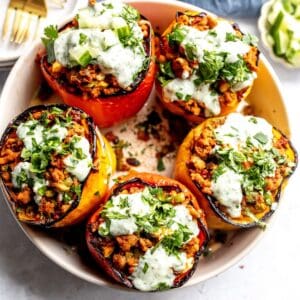 Ground turkey stuffed Peppers in a grey bowl with gold forks and plates on the side.