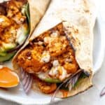 Buffalo cauliflower wraps on a white plate with a spoon to the side for serving sauce.