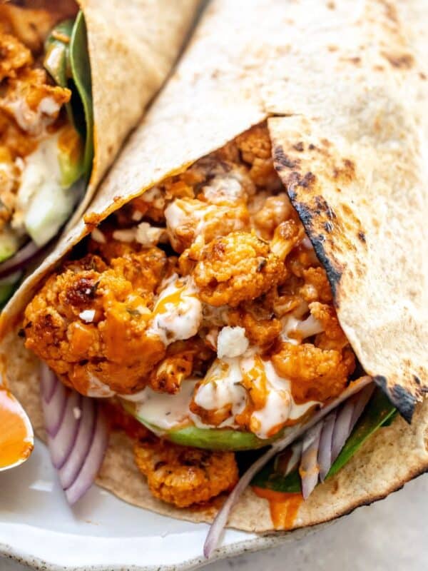 Buffalo cauliflower wraps on a white plate with a spoon to the side for serving sauce.