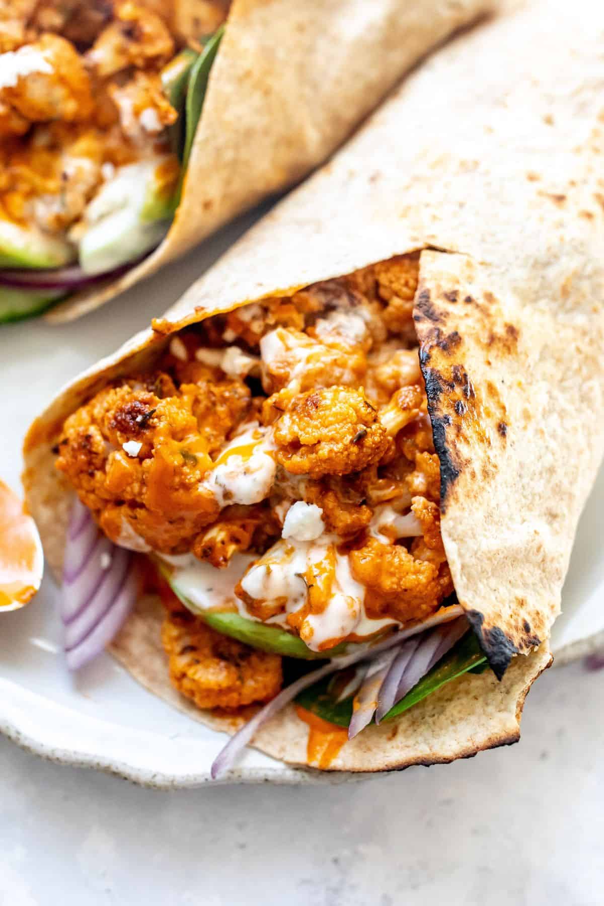 Up close photo of buffalo cauliflower wraps with drizzles of ranch on them and a spoon. 