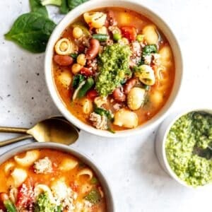 Minestrone Soup with Ground Turkey in white ceramic bowls with pesto to the side.