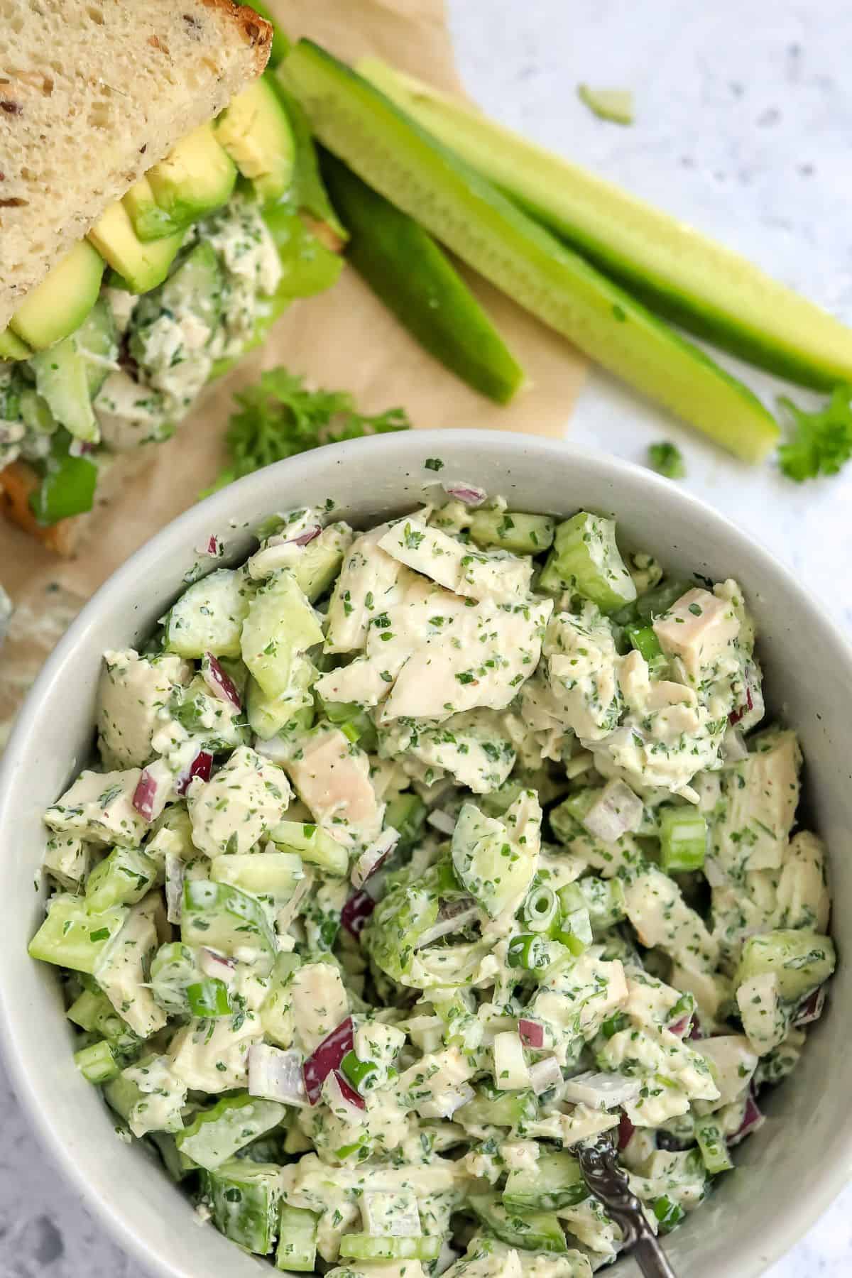 White bowl filled with green goddess  chicken salad in it and a sandwich to the side. 